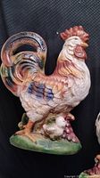 Glazed ceramic rooster figurine with two chicks and grapes, front view.