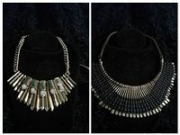 Two vintage necklaces displayed on black velvet, one with gold-tone geometric shapes and other features black beads with gold-tone bars