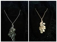 Photo showing two vintage necklaces on black display stands. Left necklace has darker metallic teardrop pendants on silver-tone chain, right necklace has light-colored pendant on gold-tone chain.