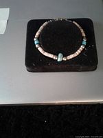 Full view of bracelet showing shell and turquoise beads on black velvet display.