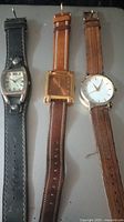 Photo of three ladies wrist watches laid flat with visible leather bands and different case shapes and dial colors.