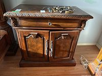 Front view showing wood grain, drawer, and double doors with silver-tone handles, top edge carving and items placed on top (not included).