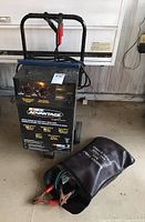 Front view of Nascar Advantage battery charger with booster cables in bag on floor.