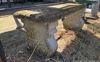 Full side view of outdoor concrete bench showing textured and moss-covered surface with ornate carved legs.
