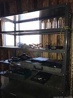 Shelving unit with assorted tools including drills, pipe wrench, drill case, and collectible glass bottles on top shelves