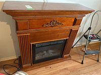 Front view of electric fireplace with wooden mantel and carved decorative accents, showing overall design and condition.