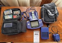 Overview of the lot showing purple Game Boy Advance, four game cartridges, two carrying cases, charger, and battery pack