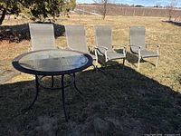 Outdoor round glass top patio table with four matching metal frame mesh fabric chairs in a yard setting.