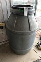 Front view of large grey resin rain barrel with a black lid and a tag hanging from upper rim.