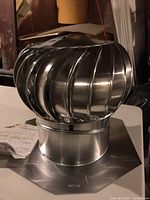 Metal turbine ventilator roof vent placed on a white surface with basement background. Instruction sheet laid nearby.