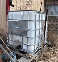 Angled front side view of the Schutz water tank showing metal cage protection, white plastic tank, and outlet valve.