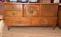 Front view of vintage sideboard showing six drawers and central cabinet door with decorative metal handle.