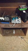 Wooden shelf holding PS1 console, Xbox 360 console, controllers, cables and stack of game cases