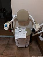 Beige padded Savaria stairlift chair with armrests and blue control button, documents on seat
