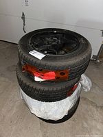 Stack of four tires mounted on black multi-spoke rims with red tape on some tires, set in a garage area.