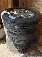 Stack of four used tires with Chevrolet branded alloy rims in garage with visible dirt and wear.