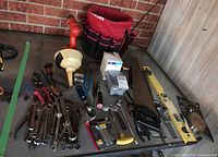 Full view of various hand tools laid out on a table including wrenches, pliers, saws, a level, staple gun, and a Husky tool holder with a Black & Decker cordless drill.
