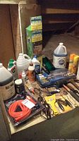 Overview of tools and cleaning supplies including boxed socket set, broom, various bottles, and hand tools on a wooden surface