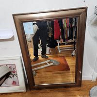 Full view of the bronze-colored framed mirror reflecting part of a room and person