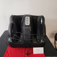 Full front view of black calf and foot massager on black table with red cloth, showing power cord and unit size.