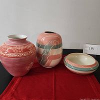 Set of three ceramic decorative pieces placed on a red fabric with mauve, pink, and pastel green patterns.