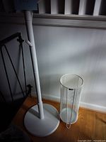 White coat rack and white mesh umbrella stand positioned on wooden floor by white wall.