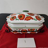 Rectangular casserole dish with lid on wrought iron stand showing poppy flower design