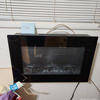 Front view of the electric fireplace showing a black glass panel with faux logs and reflection.