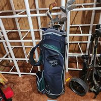 Full view of navy blue Hippo John Daly golf bag filled with assorted women's golf clubs, showing the standing legs and a shoulder strap, storage pockets.