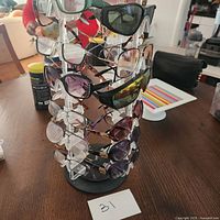 Photo of assortment of eyeglasses and shades displayed on a rotating stand on a table, showing multiple styles and colors.
