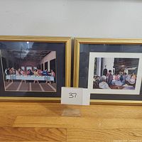 Two framed art prints side by side on a wooden surface with a small card labeled '37' between them.