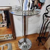 Full view of the round glass top table with chrome iron base showing clean glass and metal finish.