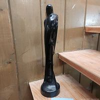 Side view of tall black glossy ceramic sculpture with abstract embracing figures, standing on a round base.