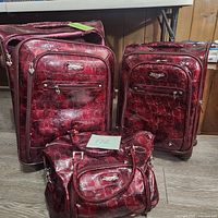Front view of two upright wheeled suitcases and a matching handbag in red croc faux leather displaying their texture, hardware, and pockets.
