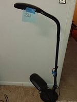 Tall black floor lamp with flexible neck and fluorescent tube bulbs attached to a round base, photographed against a wall.