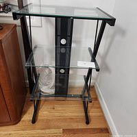 Front angle view of one metal and tempered glass display shelf showing all three clear glass shelves and metal frame.