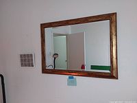 Large rectangular mirror with wide gold decorative frame hung on a wall.