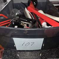 Front view of basket with assorted red, black and white kitchen utensils including tongs and peelers
