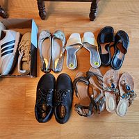 All eight pairs of shoes arranged on wooden floor, showing variety of styles and colors.