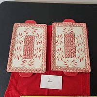 Top view of two rectangular platters placed side by side on red cloth, showing Temptations Old World Cranberry pattern with floral and geometric designs.