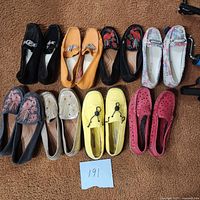 Overview of nine pairs of women's size 10 flat shoes in various colors and styles laid out on carpet.