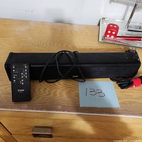 ZVOX sound bar, remote control, power cord laid on wooden surface with auction tag number 133.