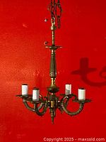 Full view of the antique French gilt brass chandelier hanging against a red wall, showing all 4 arms and the chain hanging above.
