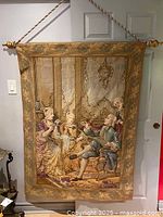 Full view of antique French tapestry hanging on a wall, showing entire design including ornate border and central scene of figures in period clothing.