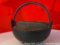 Overall view of the antique Japanese cast iron pot with wooden lid and handle on red background.