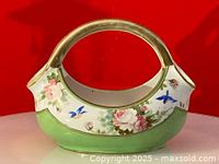 Front angle view showing hand-painted pink and white roses, blue birds, green base, and gold-tone handle.