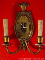 Front view of antique wall sconce showing ornate oval backplate and two arm candle holders.