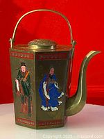 Front left side of the hexagonal brass teapot showing two hand-painted traditional Asian figures, one in green robes and one in blue robes.