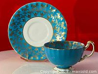 Side view of turquoise Aynsley teacup and saucer with gold leaf decoration, showing cup handle and saucer design.