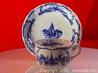 Teacup placed in front of saucer showing detailed blue sailboat and windmill scene with decorative border on white porcelain